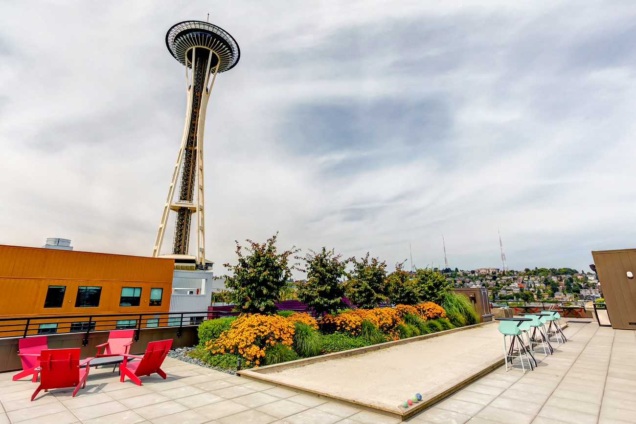 A rooftop patio with red chairs and a pool table with the Seattle Space Needle in the background